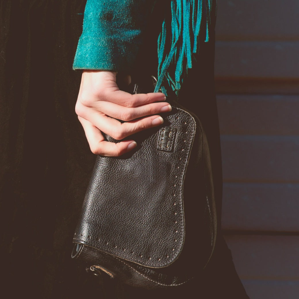 A woman holding a black Priscilla purse with tassels from the Bed Stu brand.