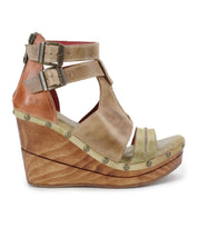The Bed Stu "Princess" is a sustainable wooden wedge sandal featuring woven strappy uppers, tan leather straps, metal studs, and a double ankle buckle system.