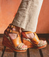 A woman wearing a pair of Bed Stu Princess wedge on a wooden floor.