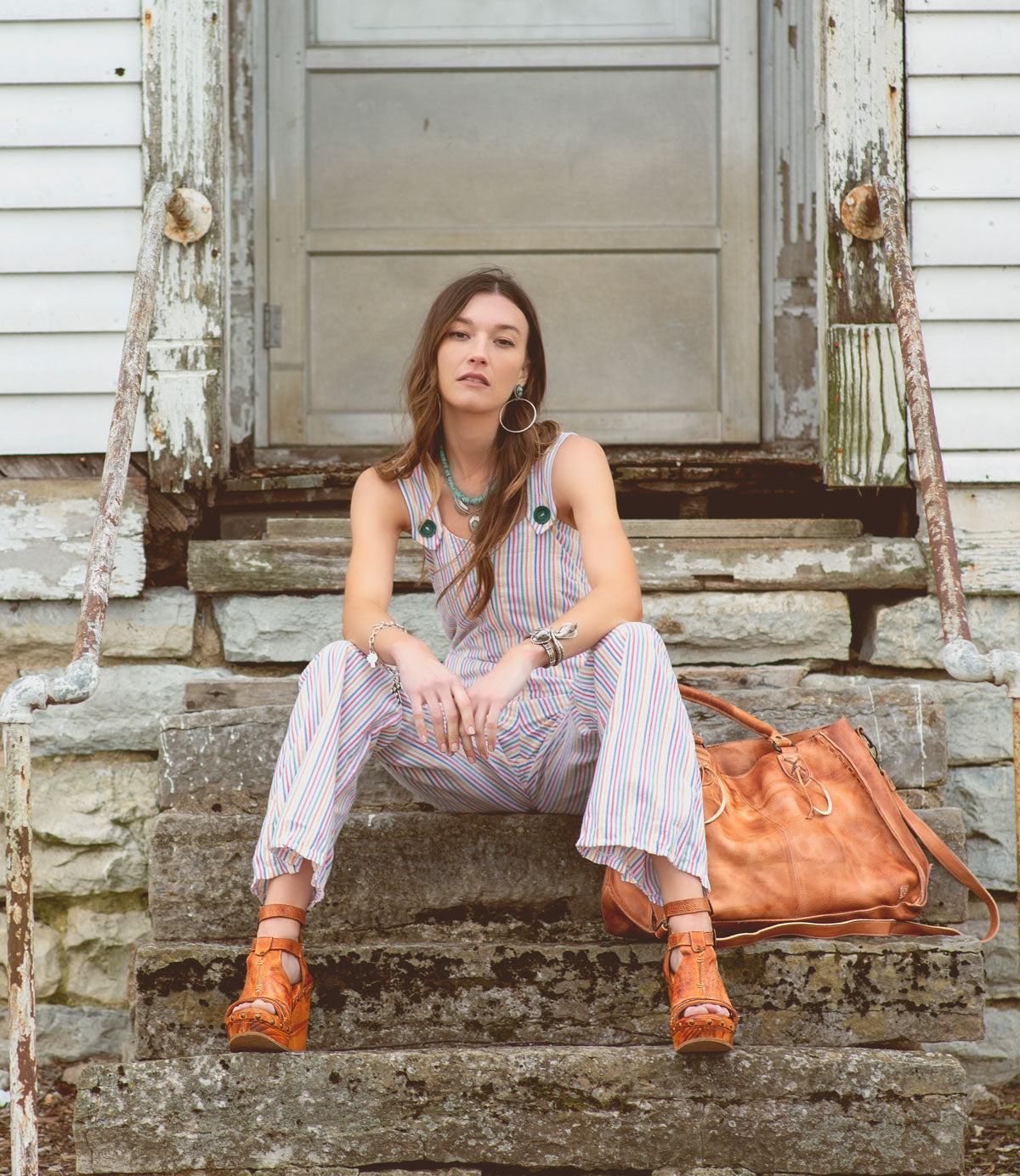 A woman sitting on the steps of an old house wearing Bed Stu Princess wedge heels.