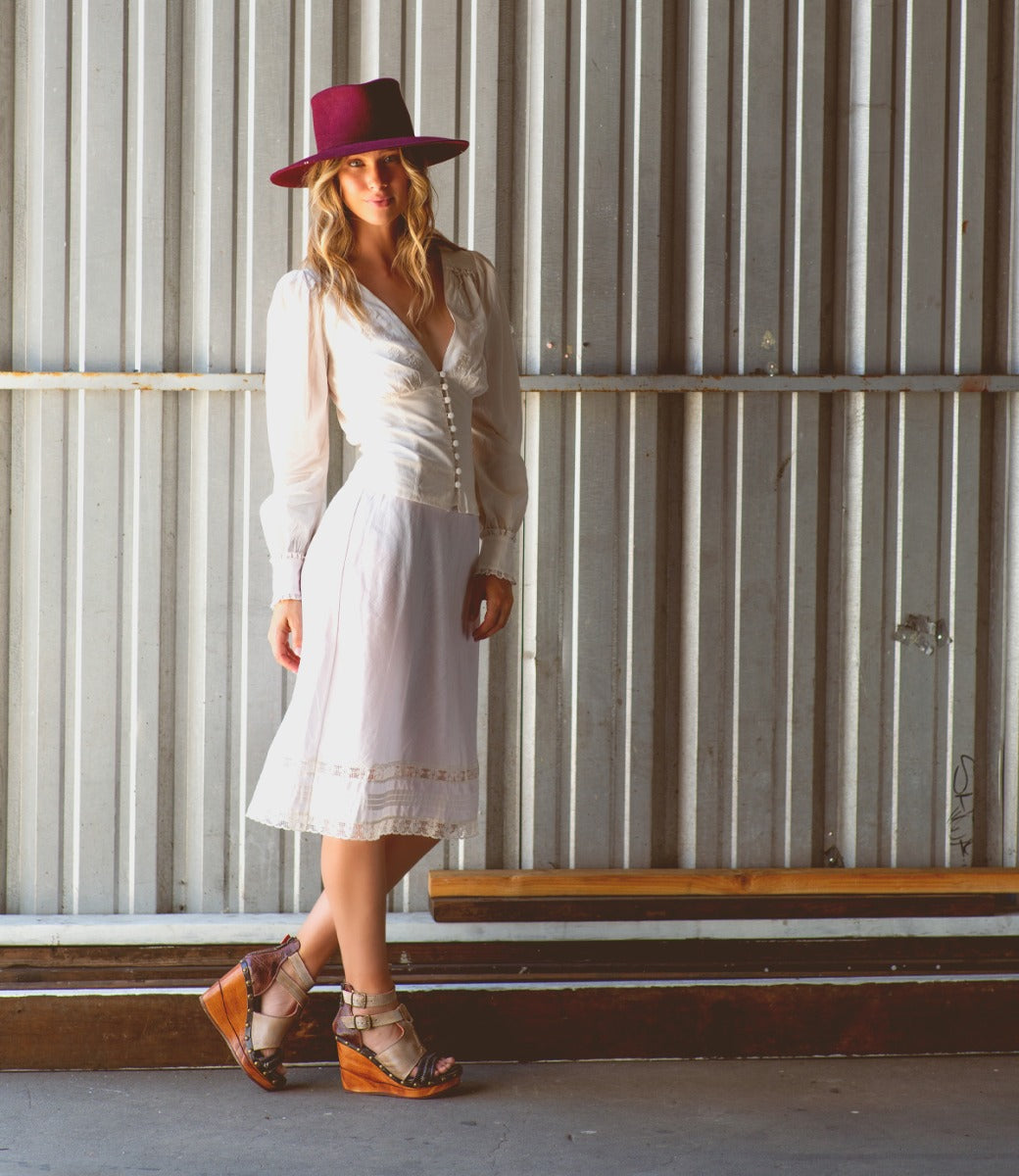 A woman wearing a white dress and Princess wooden wedge heels by Bed Stu.