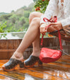 A woman is sitting on a wooden deck holding a Bed Stu Priscilla purse.
