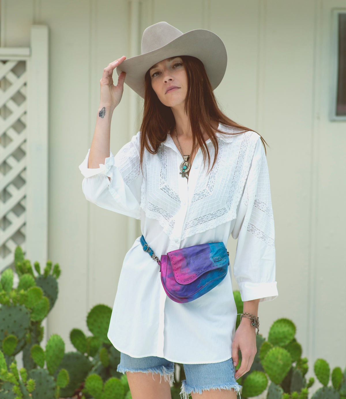 A woman in a white shirt and cactus hat wearing a tie dye Bed Stu Priscilla bag.