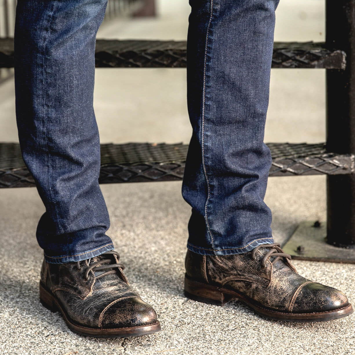 A man wearing a pair of jeans and a pair of distressed black Bed Stu Protege shoes.
