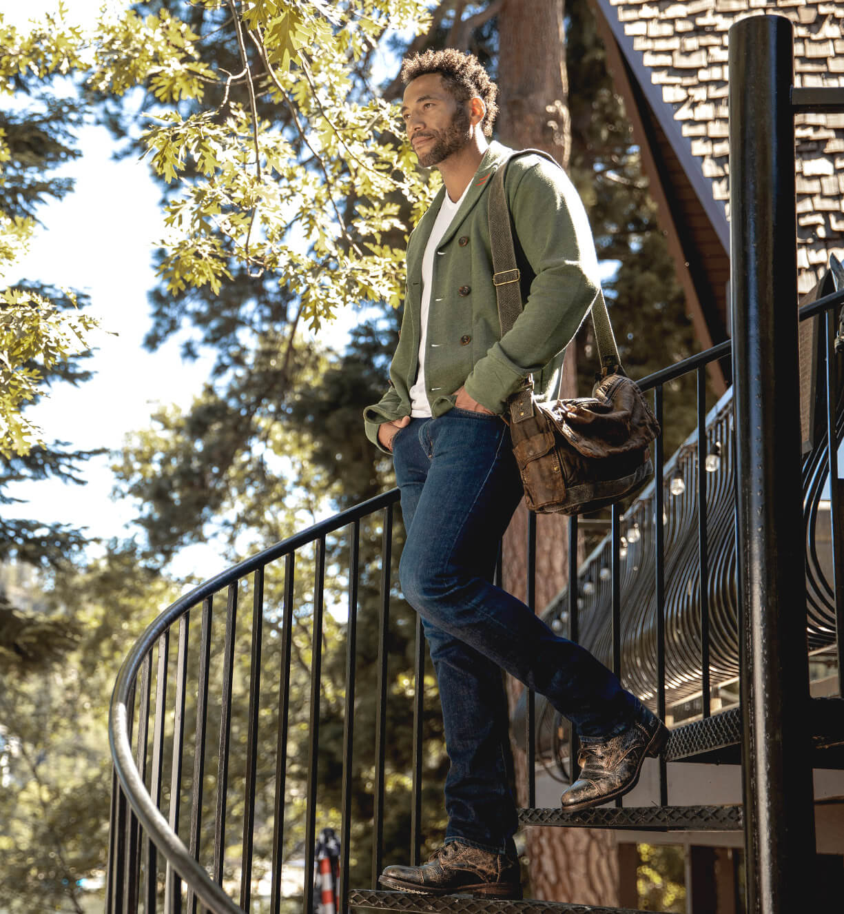 A man walking down spiral stairs while wearing green jacket, blue jeans, and black Protege boots.