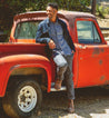 A man leaning on a red truck while wearing jean jacket, grey pants and Bed Stu Protege boots.