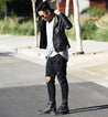 A man wearing ripped jeans, black leather jacket, and black Protege boots..