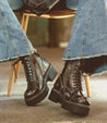A woman is sitting on a chair wearing Bed Stu Prudence Hi chunky platform combat boots.