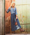 An edgy woman in a denim skirt, wearing Bed Stu Prudence Hi combat boots with a chunky platform outsole, leans against a wall.