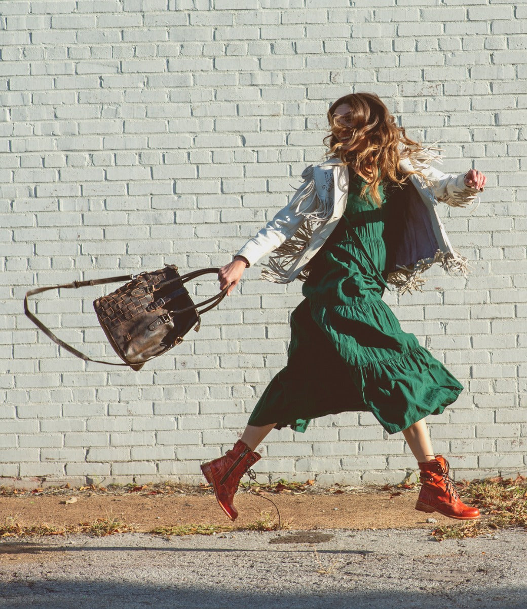A woman walking in brown jacket and green skirt holding a Rachel bag from Bed Stu.