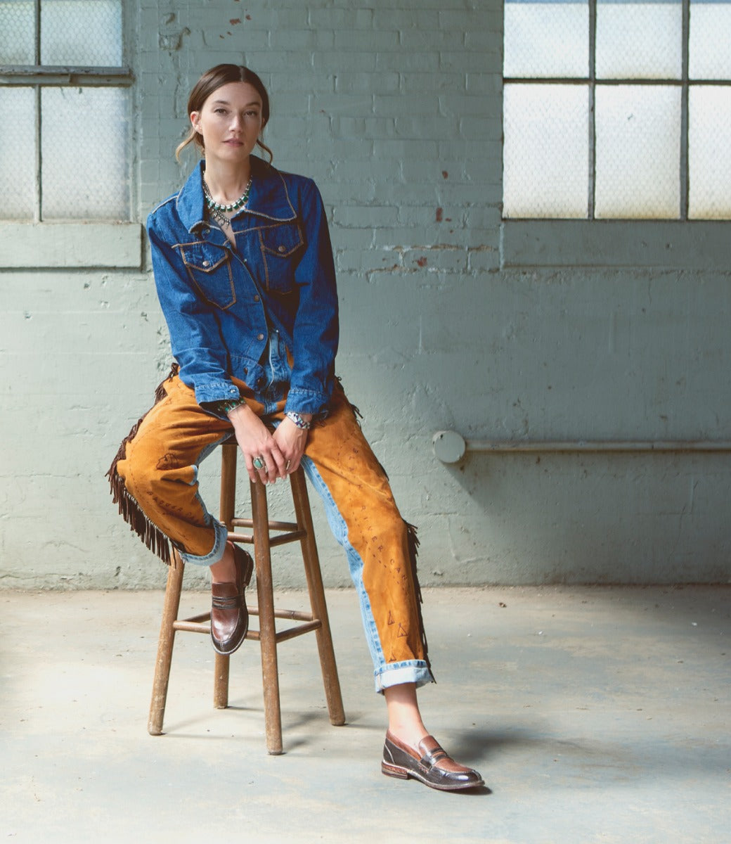 A woman sitting on a stool wearing Reina by Bed Stu and denim jacket and jeans.