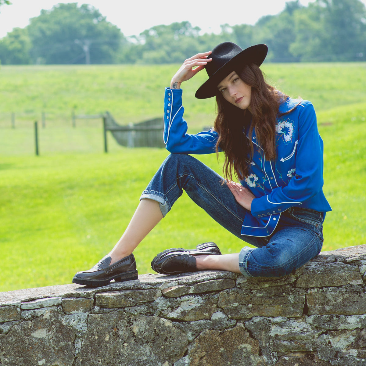 A woman in a blue shirt and hat sitting on a Bed Stu Reina III.