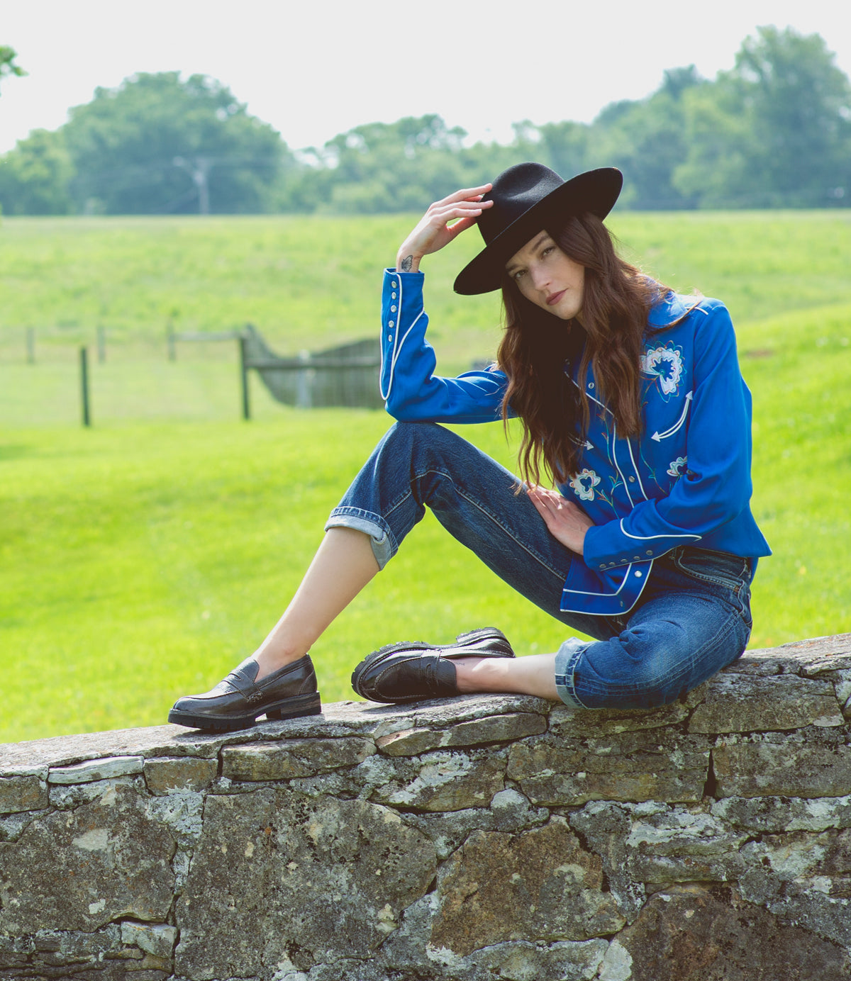 A woman in a blue shirt and hat sitting on a Bed Stu Reina III.