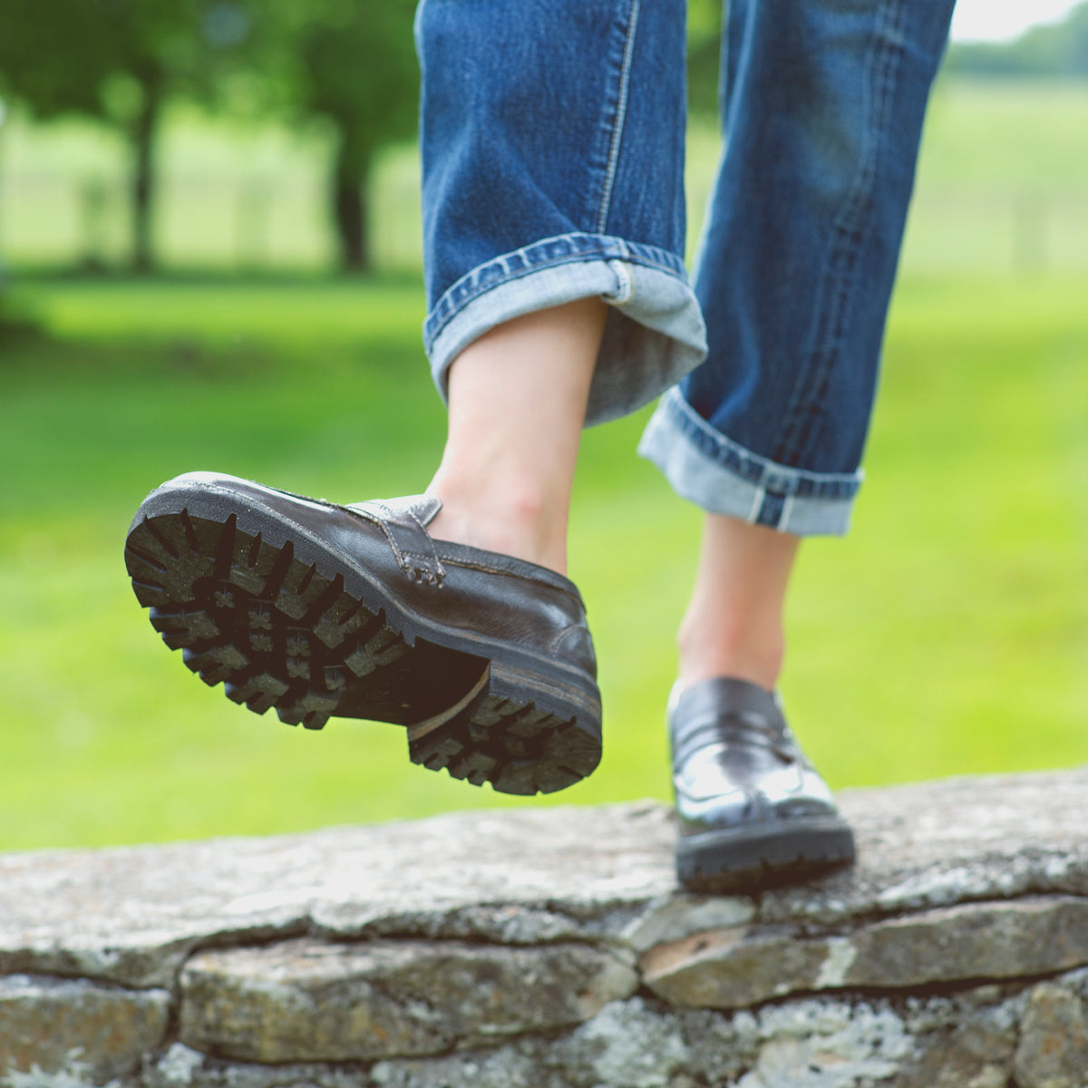 A woman wearing black loafers standing on stone wall.