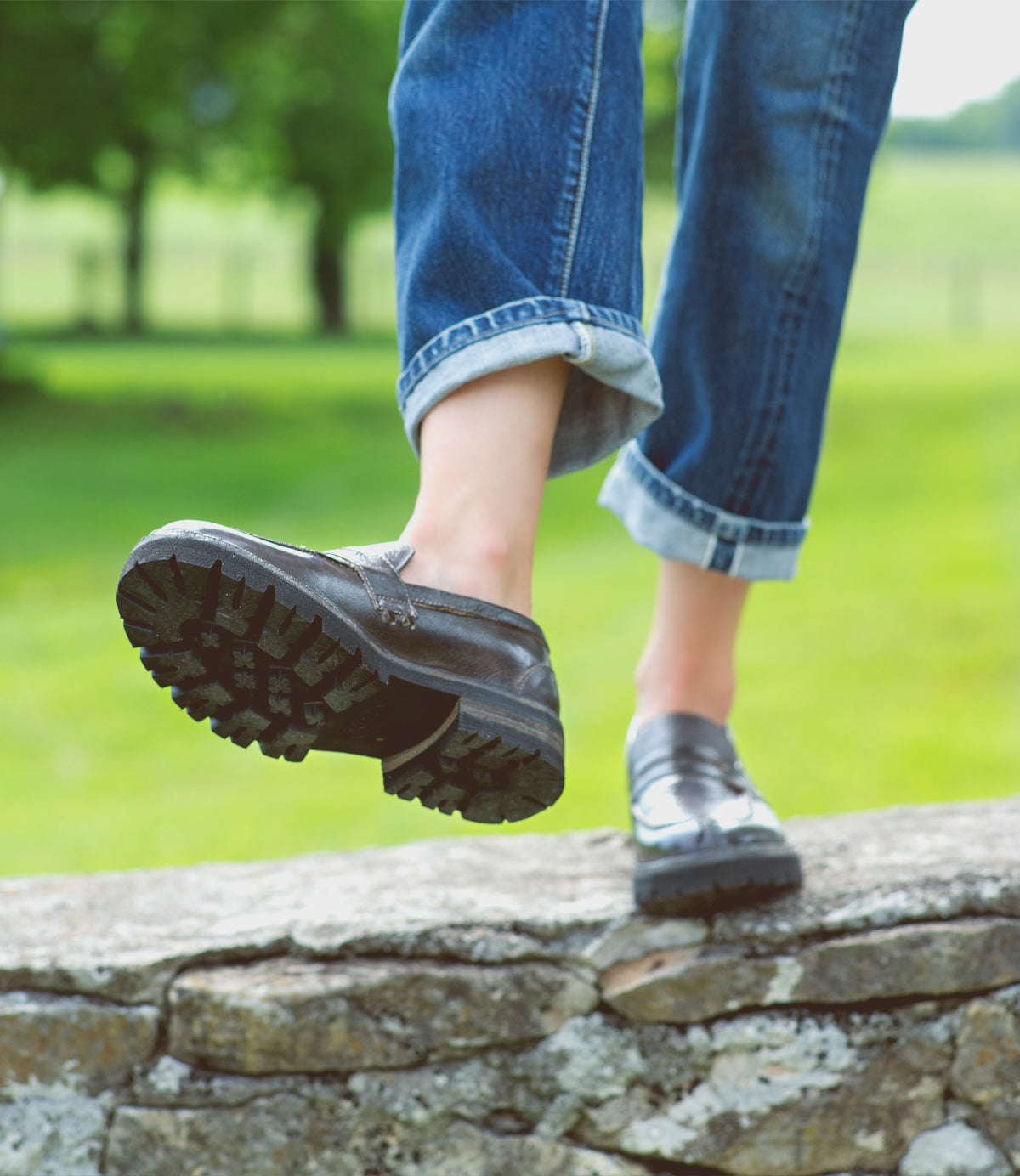 A woman wearing black loafers standing on stone wall.