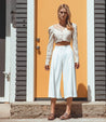 A woman in white Bed Stu Reina cropped pants standing in front of an orange door.