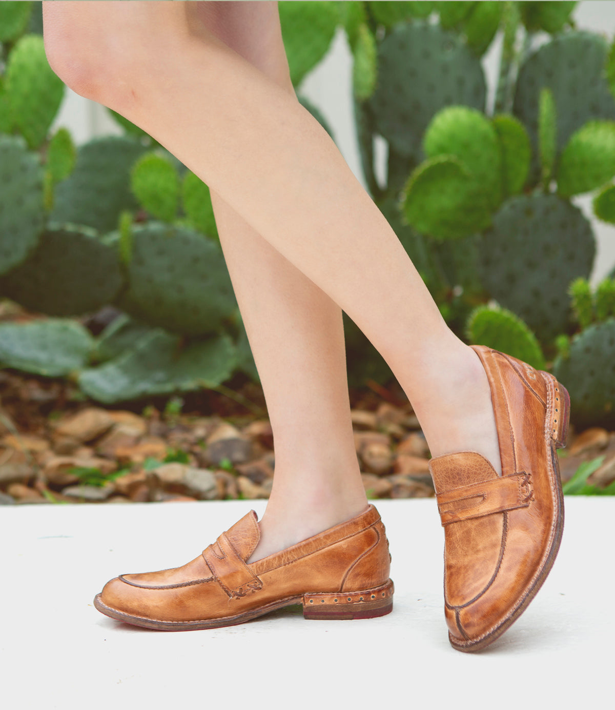 A woman wearing a pair of Bed Stu Reina tan loafers in front of a cactus.