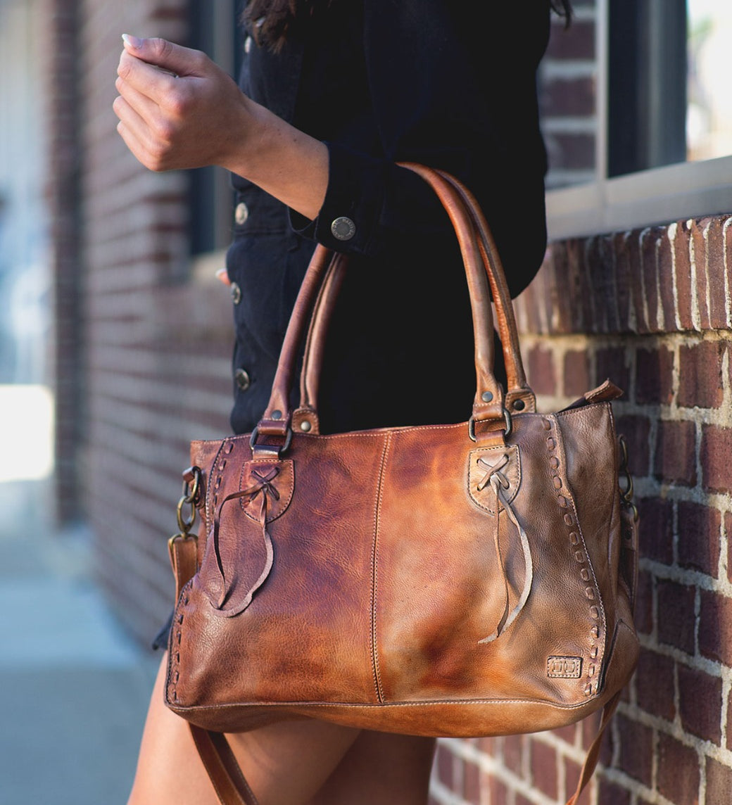 A woman is holding a Bed Stu Rockababy brown dyed leather bag.