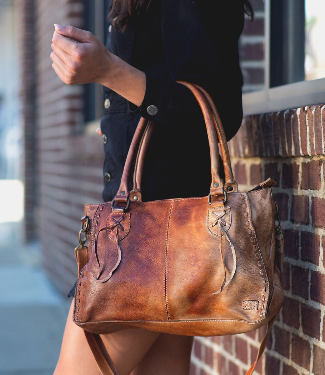 A woman is holding a Bed Stu Rockababy brown dyed leather bag.