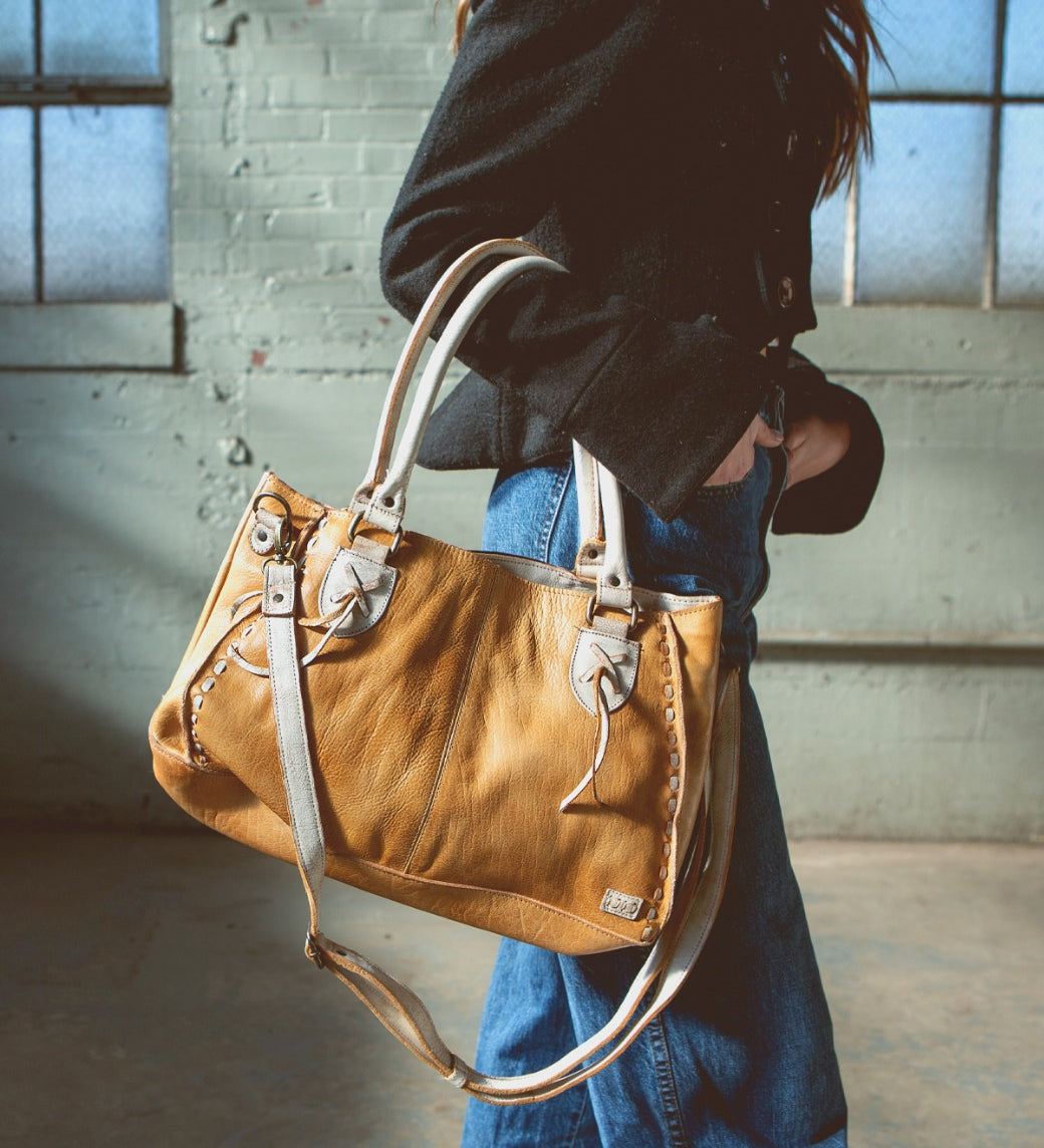 A woman is holding a Rockababy tan leather bag by Bed Stu.