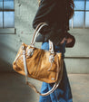 A woman is holding a Rockababy tan leather bag by Bed Stu.