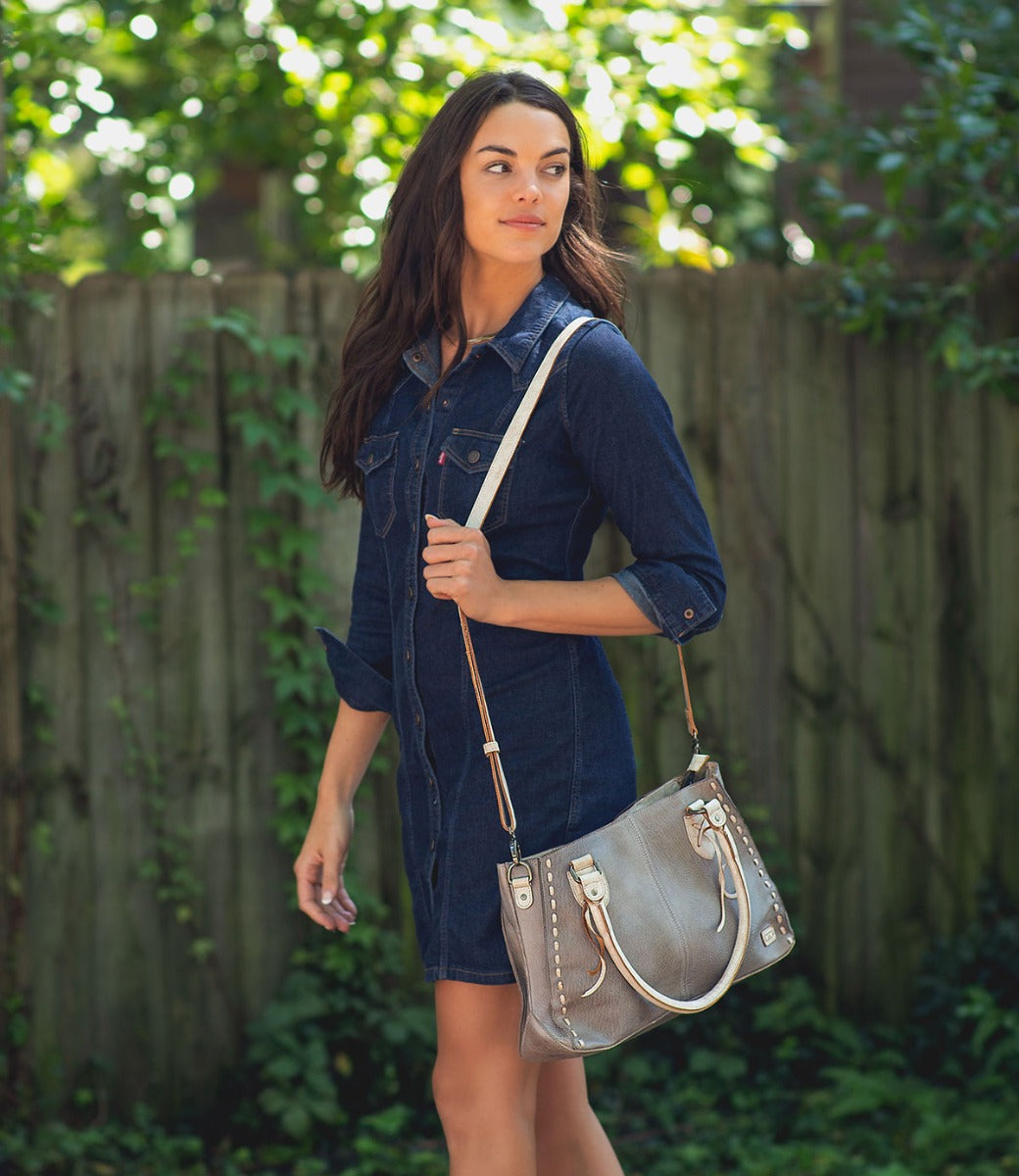 A woman in a denim dress holding a Bed Stu Rockababy grey leather bag.