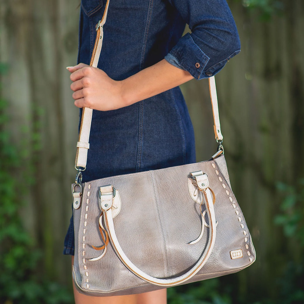 A woman in a denim dress holding a Bed Stu Rockababy bag.