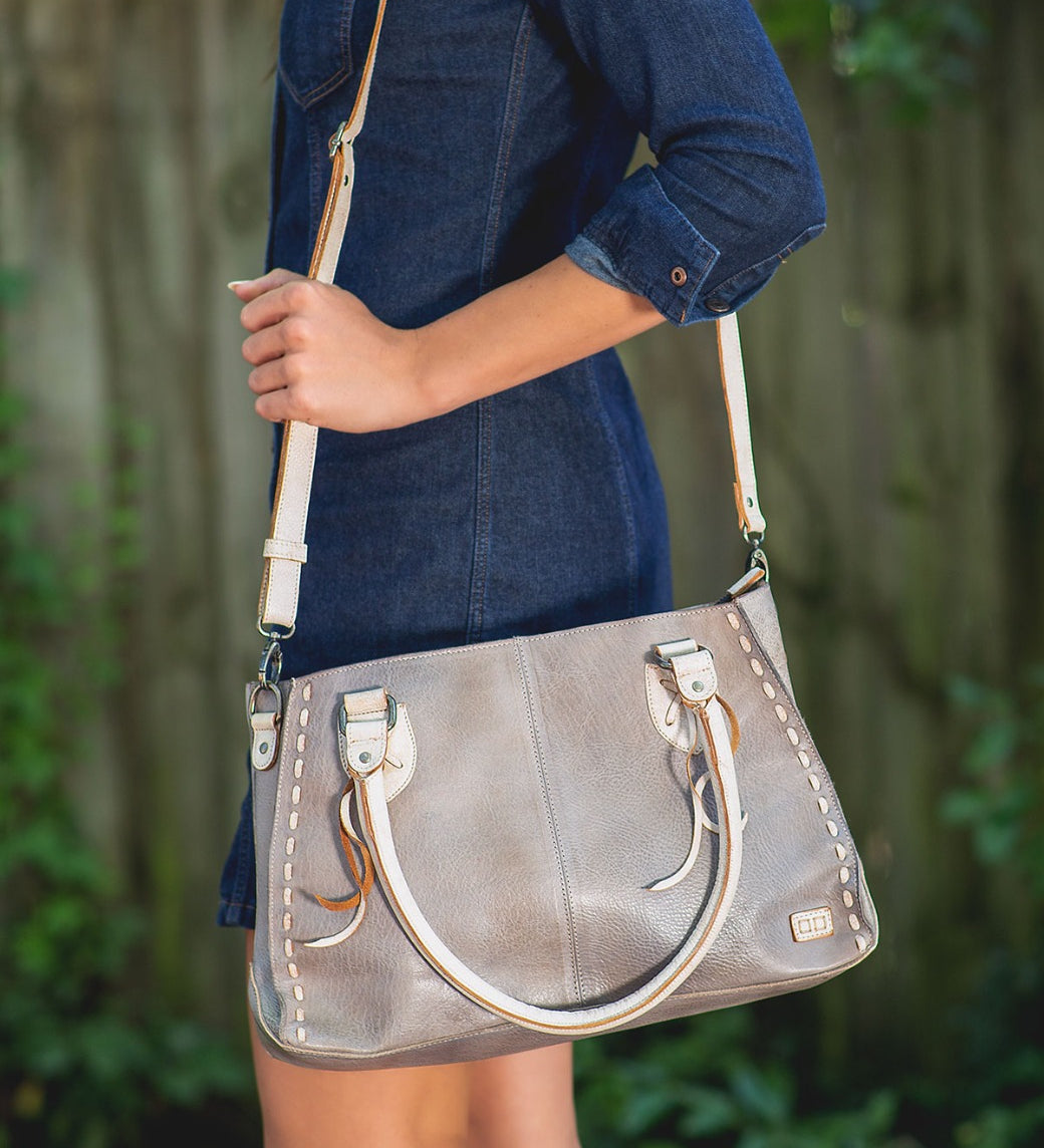 A woman in a denim dress holding a Bed Stu Rockababy bag.