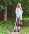 A blonde woman holding a Rockababy purse from Bed Stu in the woods.