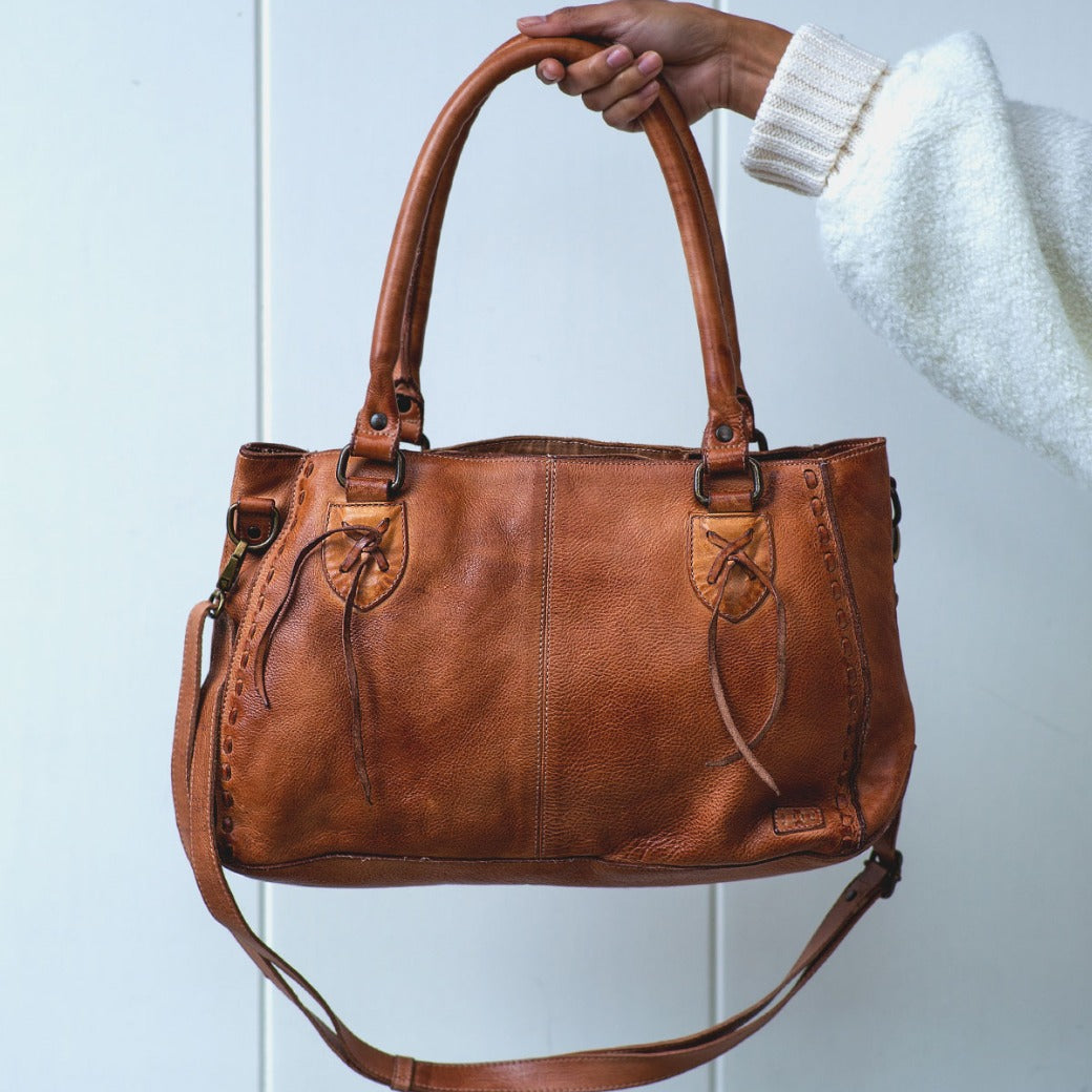 A person holding a Rockababy tan leather handbag from Bed Stu.