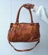 A person holding a Rockababy tan leather handbag from Bed Stu.