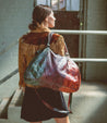 A woman is holding a colorful Bed Stu Rockaway bag.