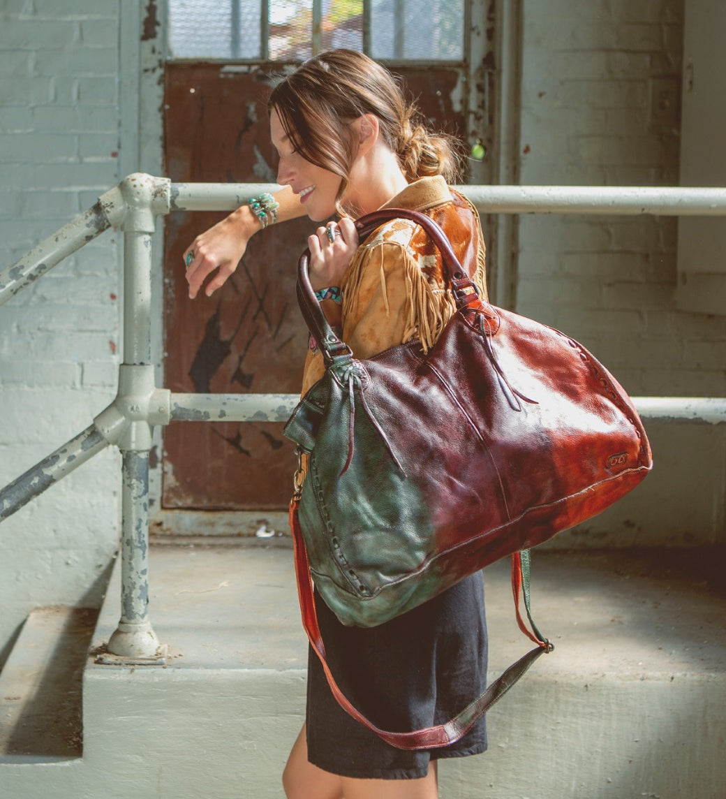 A woman is holding a colorful Rockaway leather bag by Bed Stu.
