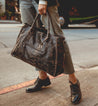 A woman walking down the street with a Bed Stu Rockaway black leather bag.