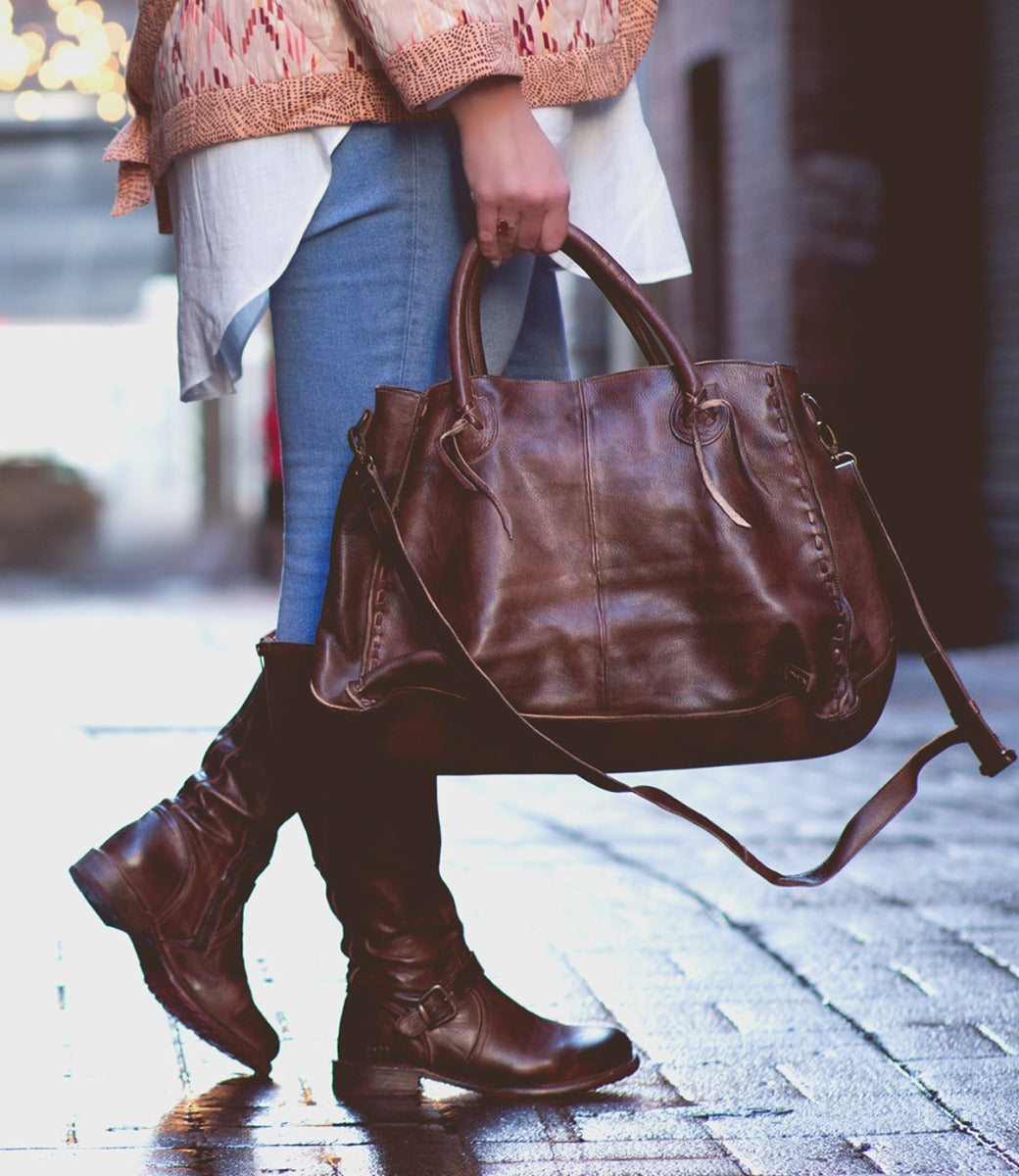 A woman carrying a Rockaway handbag by Bed Stu on a sidewalk.