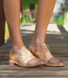 A woman wearing a pair of Bed Stu Rose shoes standing on a wooden bridge.