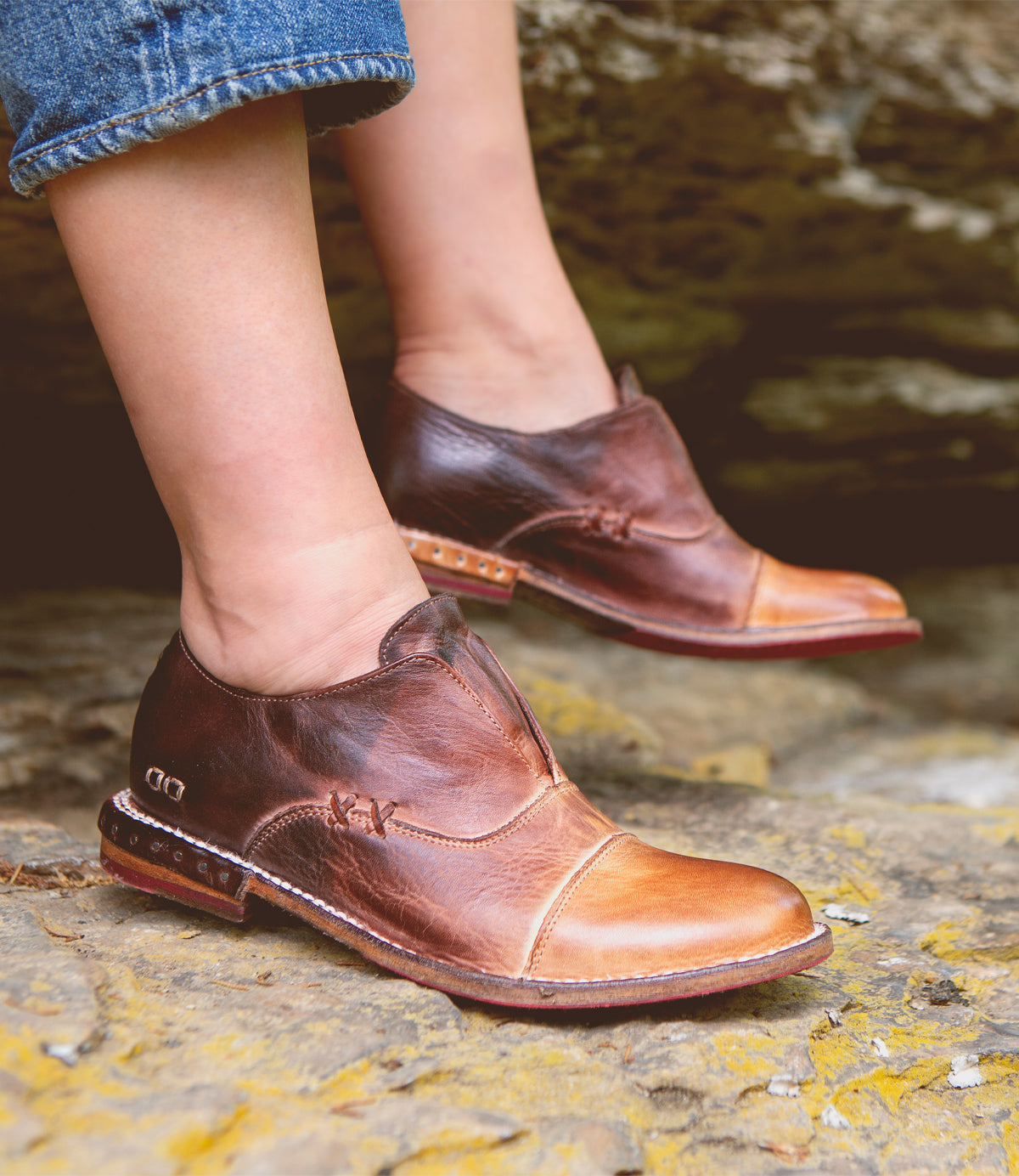 A woman's feet standing on rocks in a pair of Bed Stu Rose shoes.