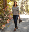 A woman wearing Rose jeans and a Bed Stu hat walks down a street.