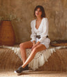 A woman in a white Rossela romper sitting on a rug. (Bed Stu)