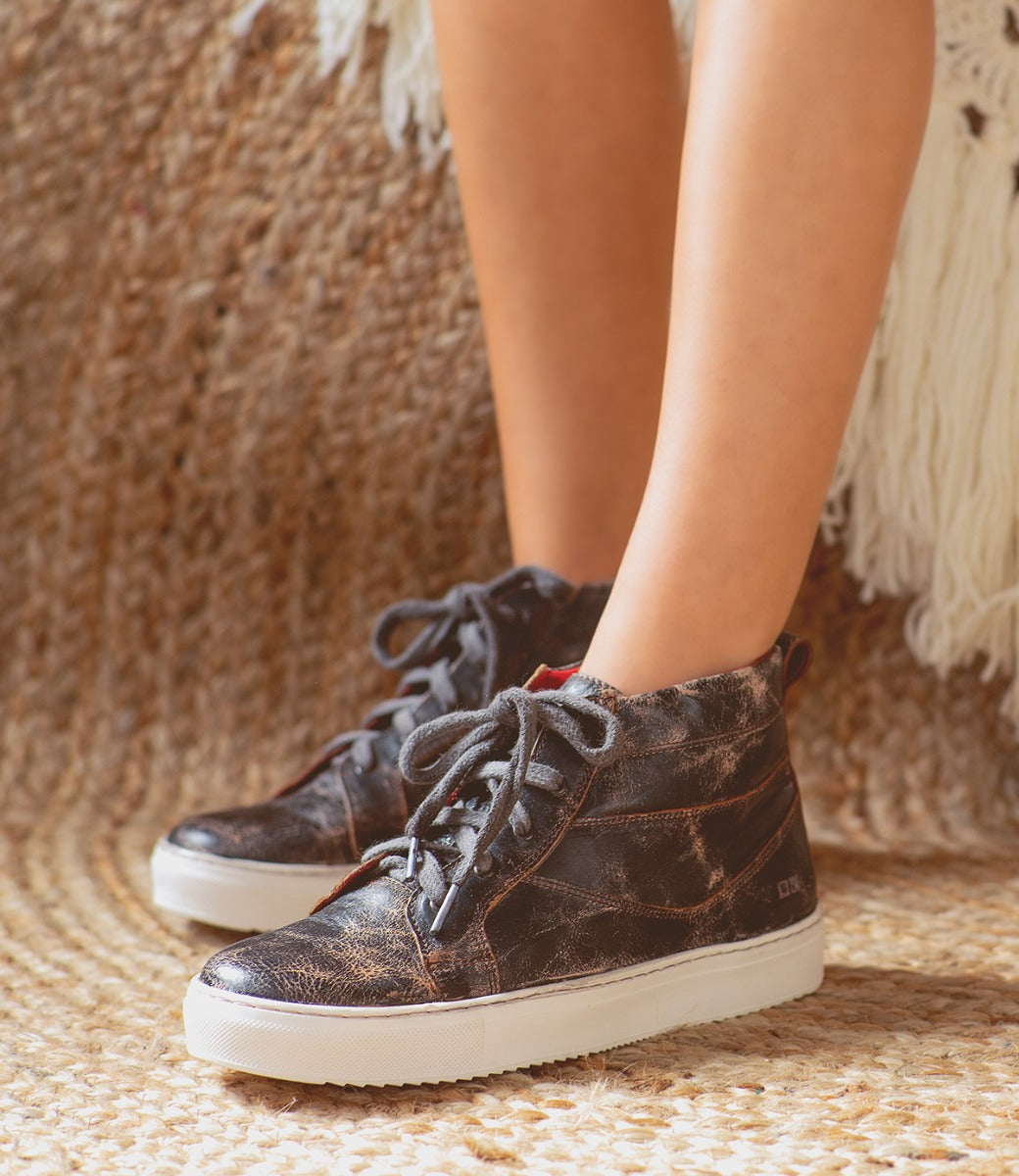 A woman wearing a pair of Bed Stu Rossela sneakers on a rug.