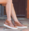 A woman wearing a brown Bed Stu Rossela crocodile high top sneaker.