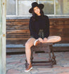 A woman wearing a black Rossela sweater and hat sitting on a wooden bench.
