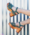 A woman's legs are posing in a pair of green Bed Stu Sabine sandals.