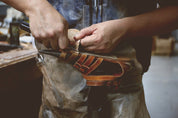 A person sharpening a tool on a grinding wheel, with sparks visible and wearing protective Bed Stu leather sandals.