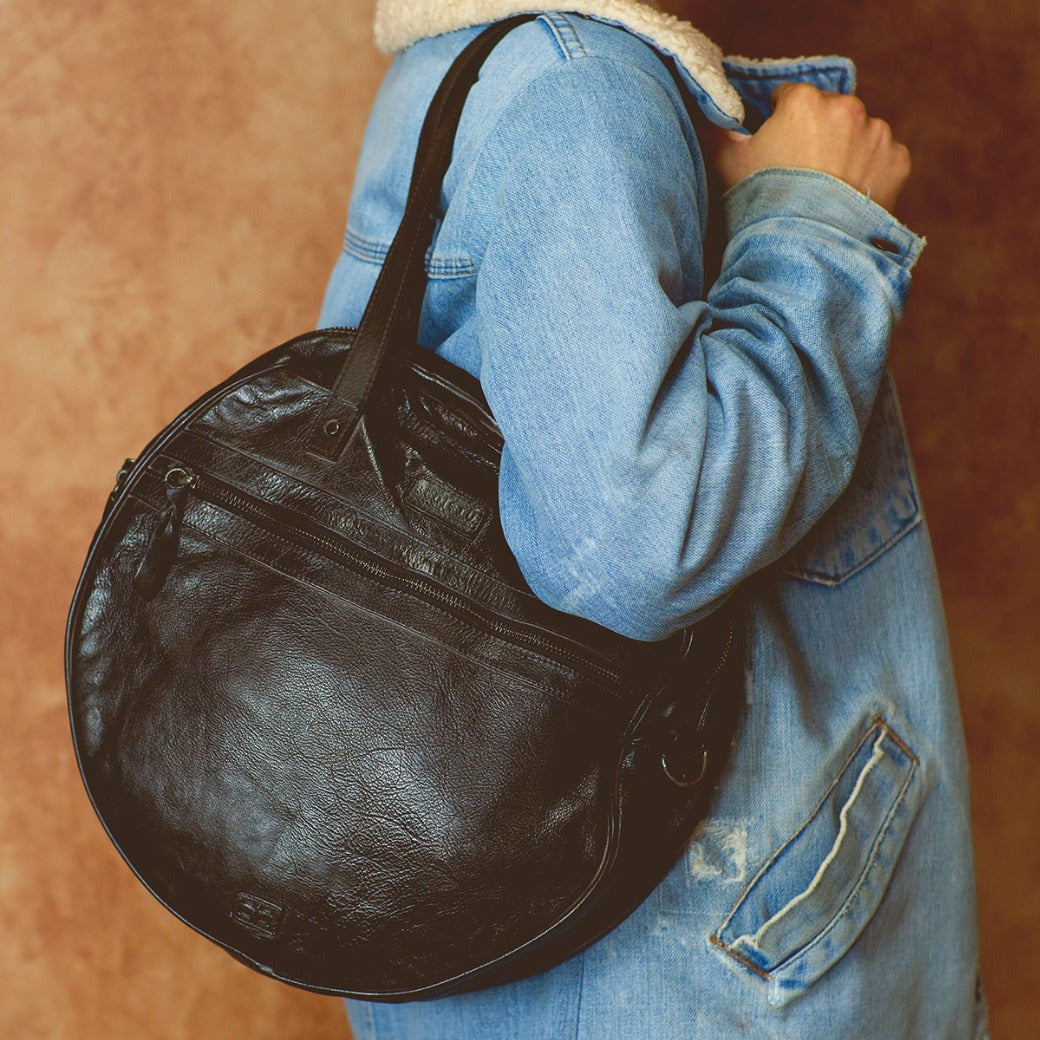 A woman wearing a denim jacket holding a black leather Saray bag by Bed Stu.