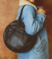 A woman wearing a denim jacket holding a black leather Saray bag by Bed Stu.