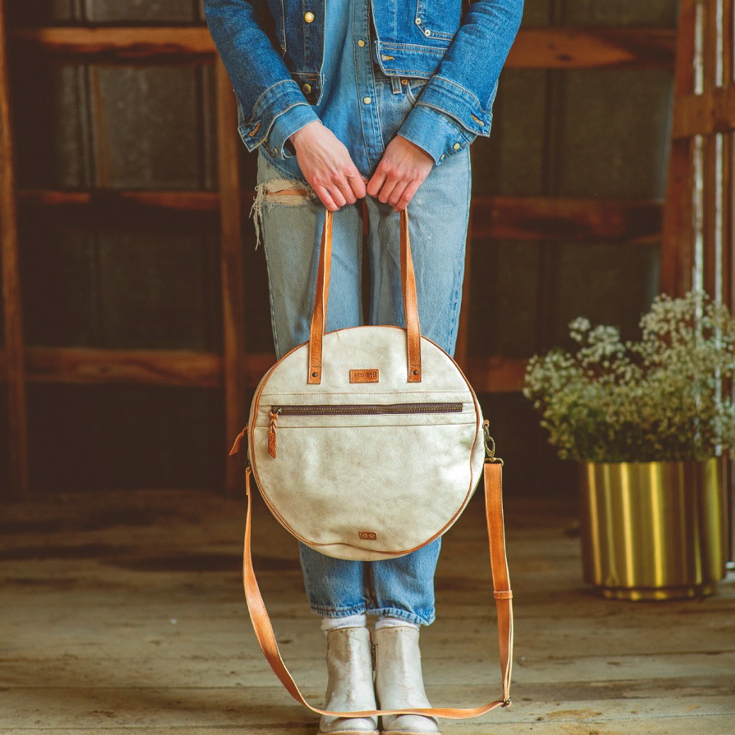 A woman wearing a denim jacket and jeans holding a Bed Stu Saray white leather purse.
