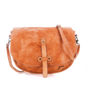 The Bed Stu Sequoia EM is a light brown vegetable-tanned leather crossbody saddle bag with a front strap closure, embossed floral pattern, and adjustable crossbody strap for comfort.