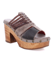 The Shantel by Bed|Stü is a women's open-toe mule sandal showcasing leather straps, metal stud accents around the sole, and a wooden block heel. Designed with a cushioned leather insole for enhanced comfort, this cheerful clog effortlessly elevates any warm-weather ensemble.