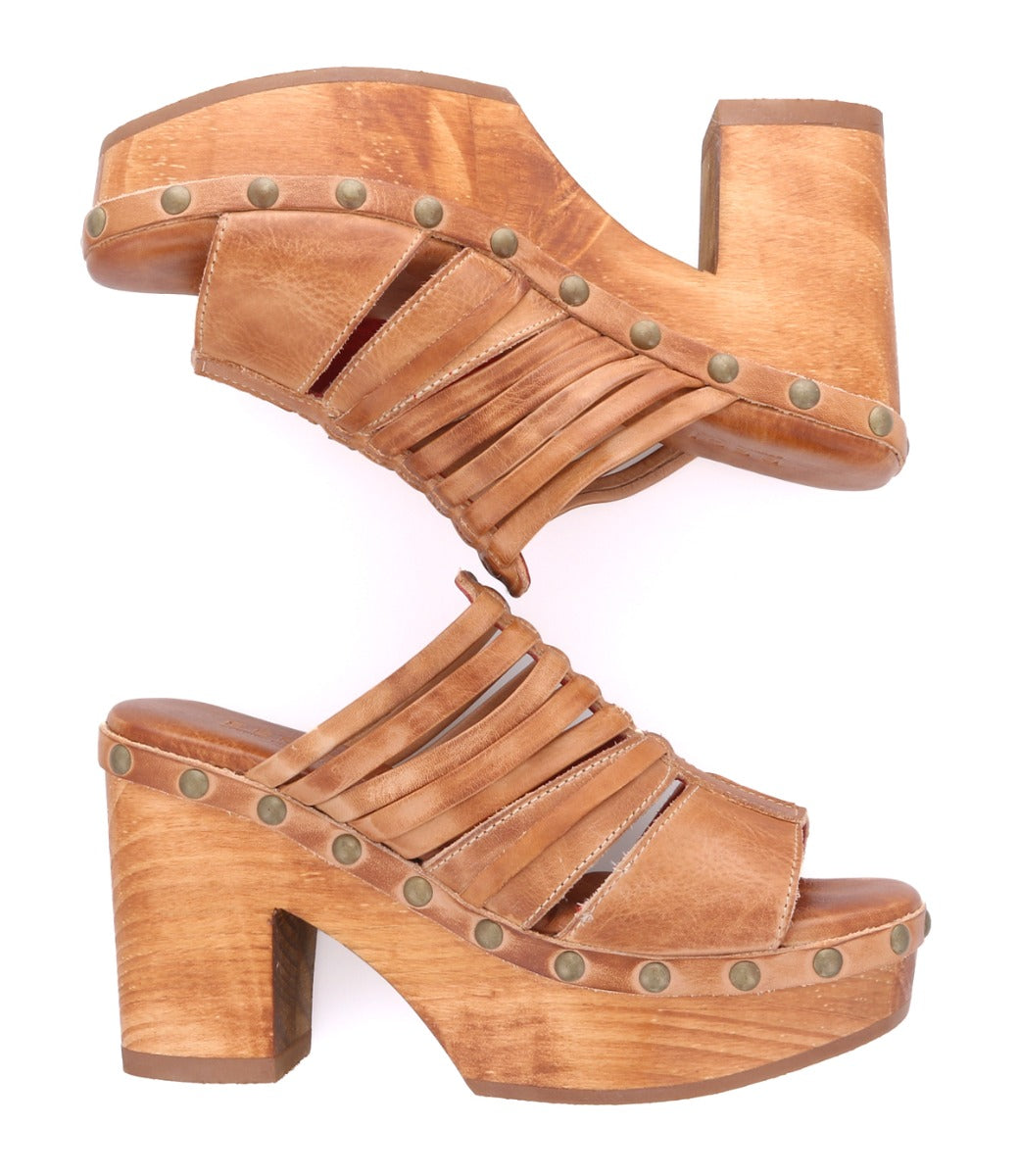 The Shantel platform clogs by Bed|Stü showcase strappy tan leather uppers, wooden soles with chunky high heels, and a cushioned leather insole for enhanced comfort. Metal stud accents line the edges of these stylish clogs, displayed against a white background.